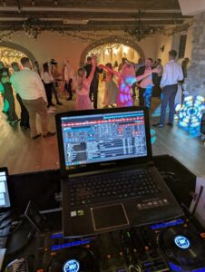 DJ weselny ZABAWIŚCI rozmawiający z gościem przy konsolecie, przyjmujący dedykację muzyczną z uśmiechem.